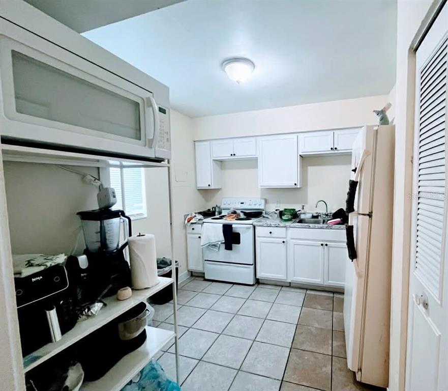 A kitchen features white cabinets, white appliances, tiled flooring, and a metal shelving unit — 5885 DAHLIA DRIVE UNIT 29/115, ORLANDO, FL