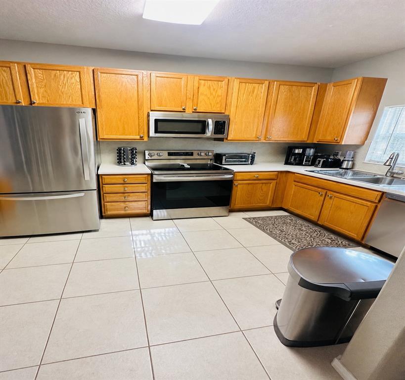 A kitchen features light wood cabinets, stainless steel appliances, and large beige floor tiles — 1852 77TH DRIVE, VERO BEACH, FL