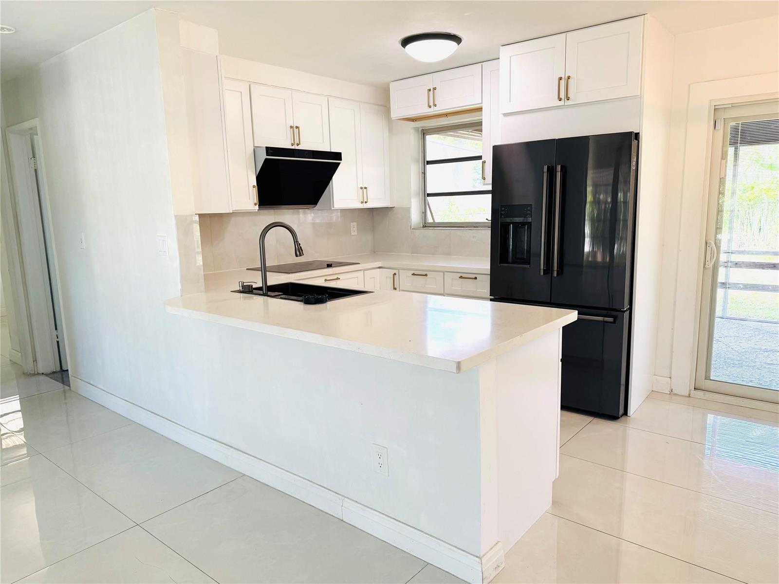 A modern kitchen features white cabinets, a black refrigerator, and a white quartz peninsula — 1521 NW 62nd Terrace, Margate FL 33063, MARGATE, FL