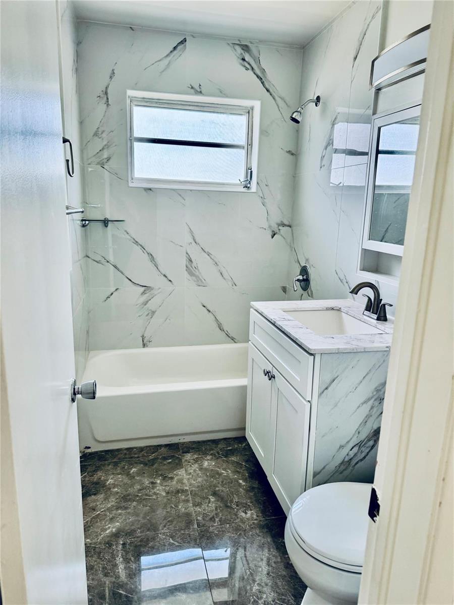 A bathroom features a white vanity, a bathtub with marble-patterned tile, and dark flooring — 1521 NW 62nd Terrace, Margate FL 33063, MARGATE, FL