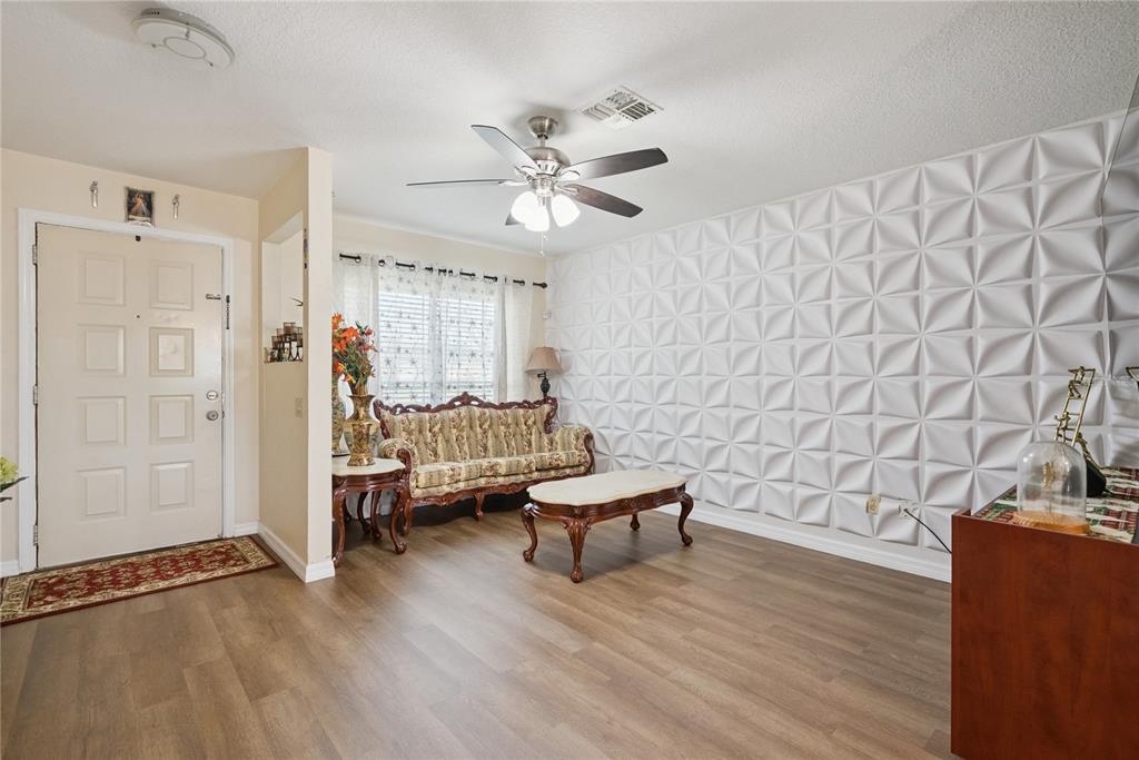 A living room features wood-look flooring, a textured white accent wall, and a ceiling fan — 1405 CORONET DRIVE, DELTONA, FL
