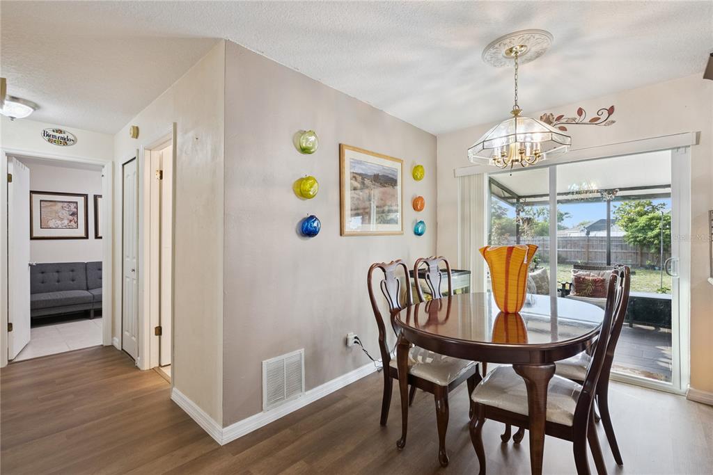 A dining room with a round wooden table, chairs, glass wall art, and sliding doors — 1405 CORONET DRIVE, DELTONA, FL