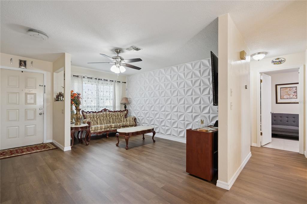 A living room features wood-look flooring, a textured accent wall, and a traditional sofa — 1405 CORONET DRIVE, DELTONA, FL