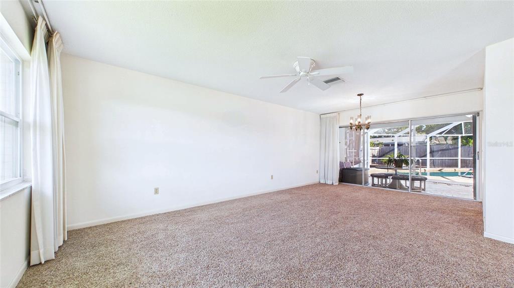 A carpeted living room features a ceiling fan, white walls, and sliding glass patio doors — 1067 44TH AVENUE NE, ST PETERSBURG, FL