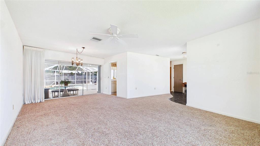 A spacious living room with beige carpeting, a ceiling fan, and sliding glass patio doors — 1067 44TH AVENUE NE, ST PETERSBURG, FL