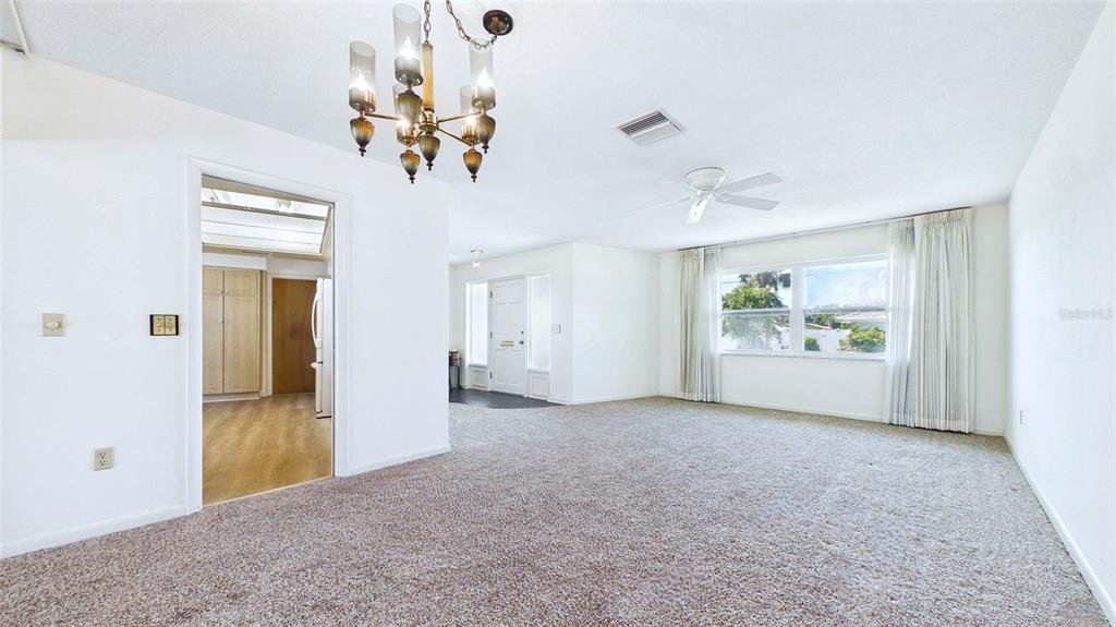 A carpeted living room features a chandelier, a ceiling fan, and a doorway to a kitchen — 1067 44TH AVENUE NE, ST PETERSBURG, FL