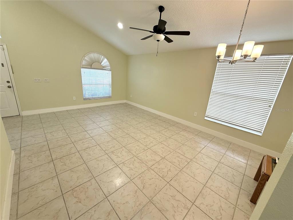 An empty room features light-colored tile flooring, a vaulted ceiling with a fan, and windows — 4207 ANDOVER CAY BOULEVARD, ORLANDO, FL