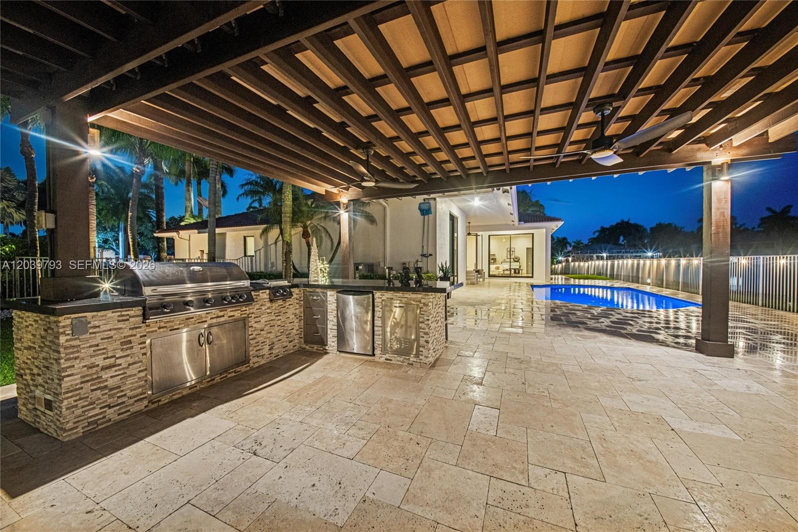 An outdoor kitchen with a grill and stone facade sits under a pergola by a pool — 935 Gulfstream Ct, Weston FL 33327, WESTON, FL