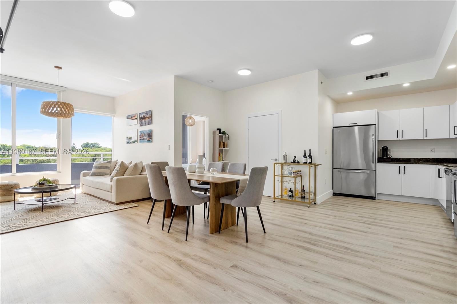 An open-concept living and dining area features light wood flooring, white cabinetry, and a balcony — 3250 Grand Ave # 507, Miami FL 33133, MIAMI, FL