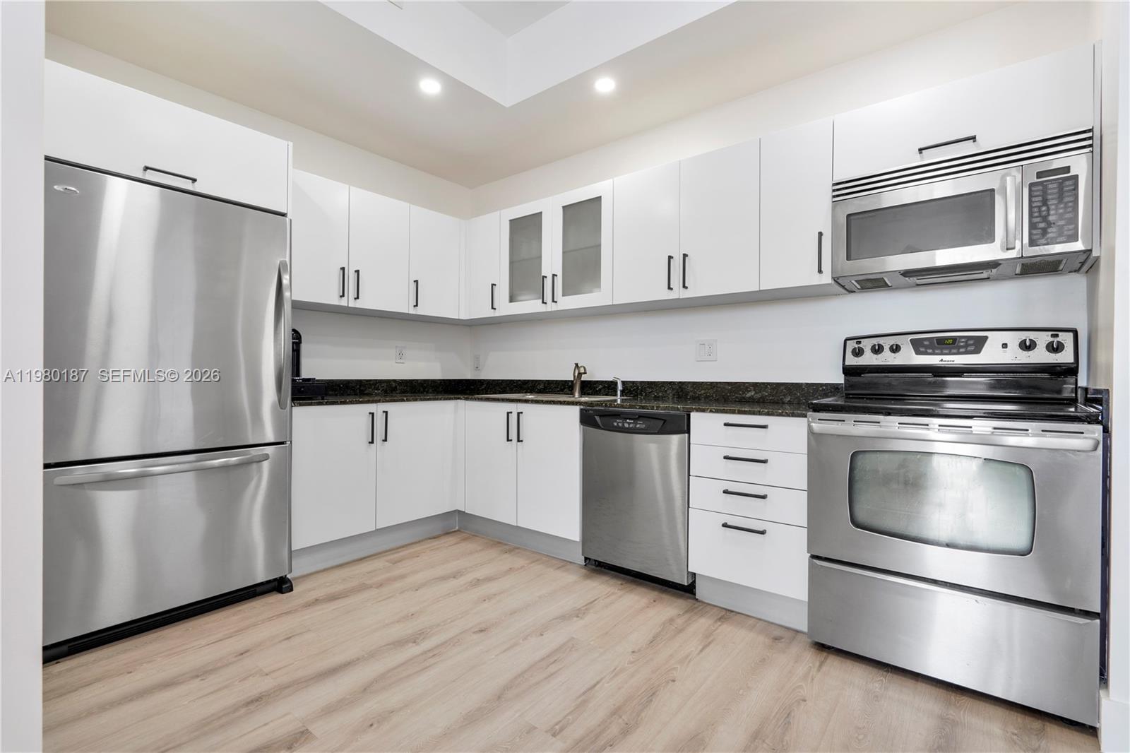A modern kitchen features white cabinets, stainless steel appliances, and dark granite countertops — 3250 Grand Ave # 507, Miami FL 33133, MIAMI, FL