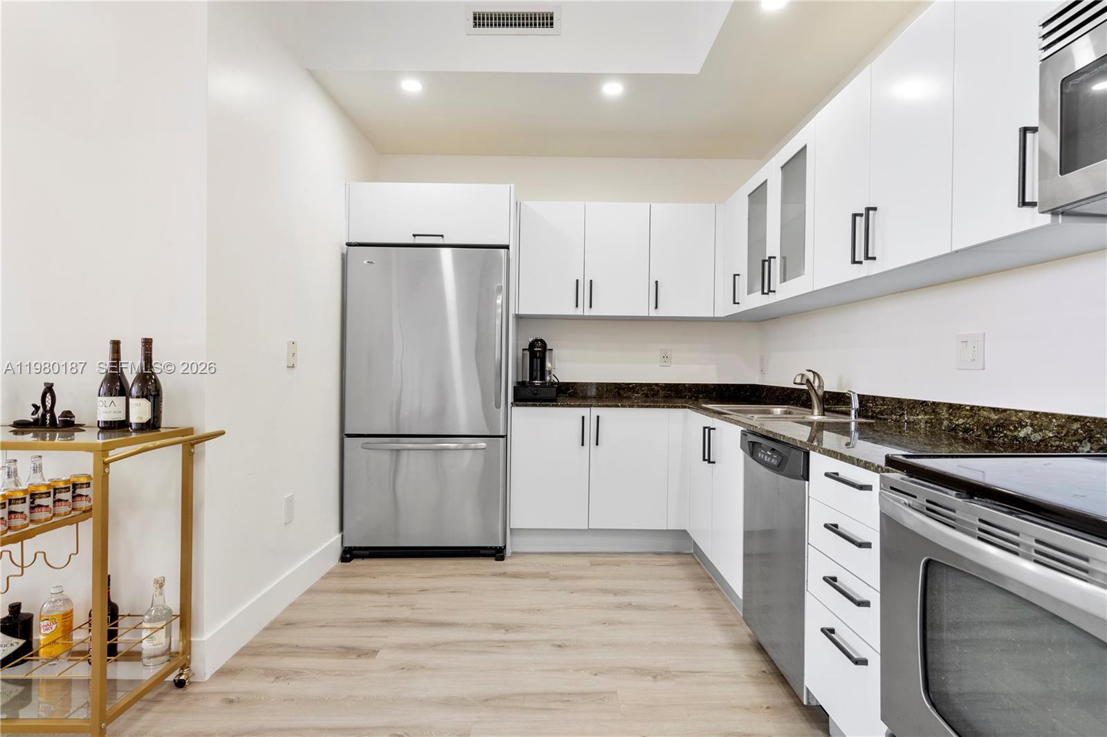 A modern kitchen features white cabinets, stainless steel appliances, dark countertops, and a gold bar cart — 3250 Grand Ave # 507, Miami FL 33133, MIAMI, FL