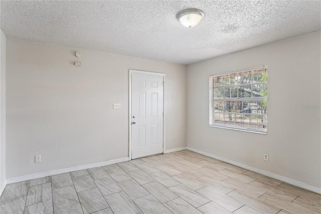 An empty room with light-colored walls, tile flooring, a white door, and a window — 9608 N 10TH STREET, TAMPA, FL