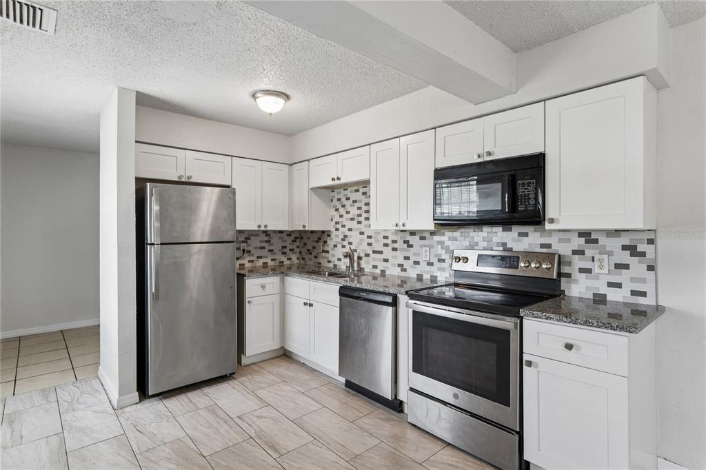 A kitchen features white cabinets, stainless steel appliances, granite countertops, and a mosaic tile backsplash — 9608 N 10TH STREET, TAMPA, FL