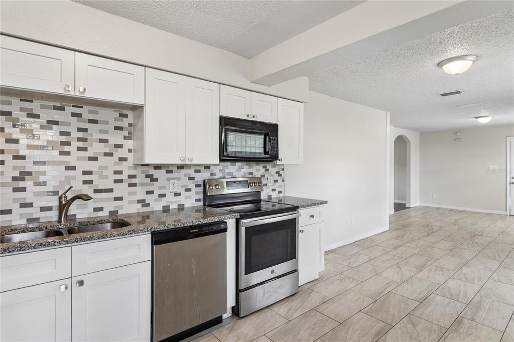 A kitchen with white cabinets, stainless steel appliances, granite countertops, and a mosaic tile backsplash — 9608 N 10TH STREET, TAMPA, FL