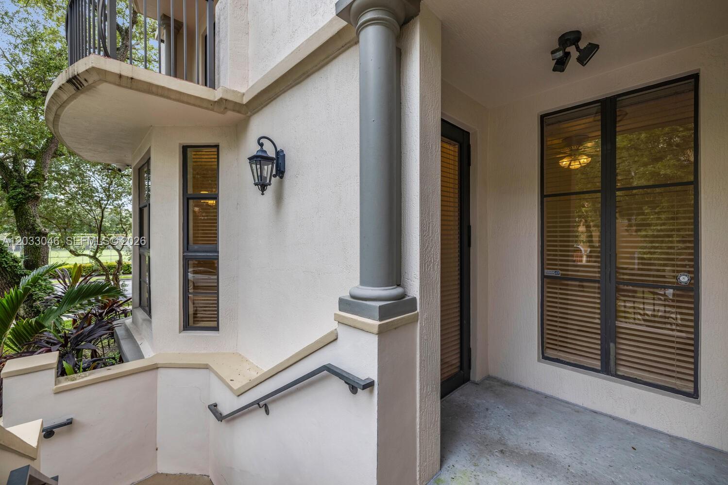 A concrete porch features a dark-framed glass door, a grey column, and a metal railing — 1650 Galiano St, Coral Gables FL 33134, CORAL GABLES, FL