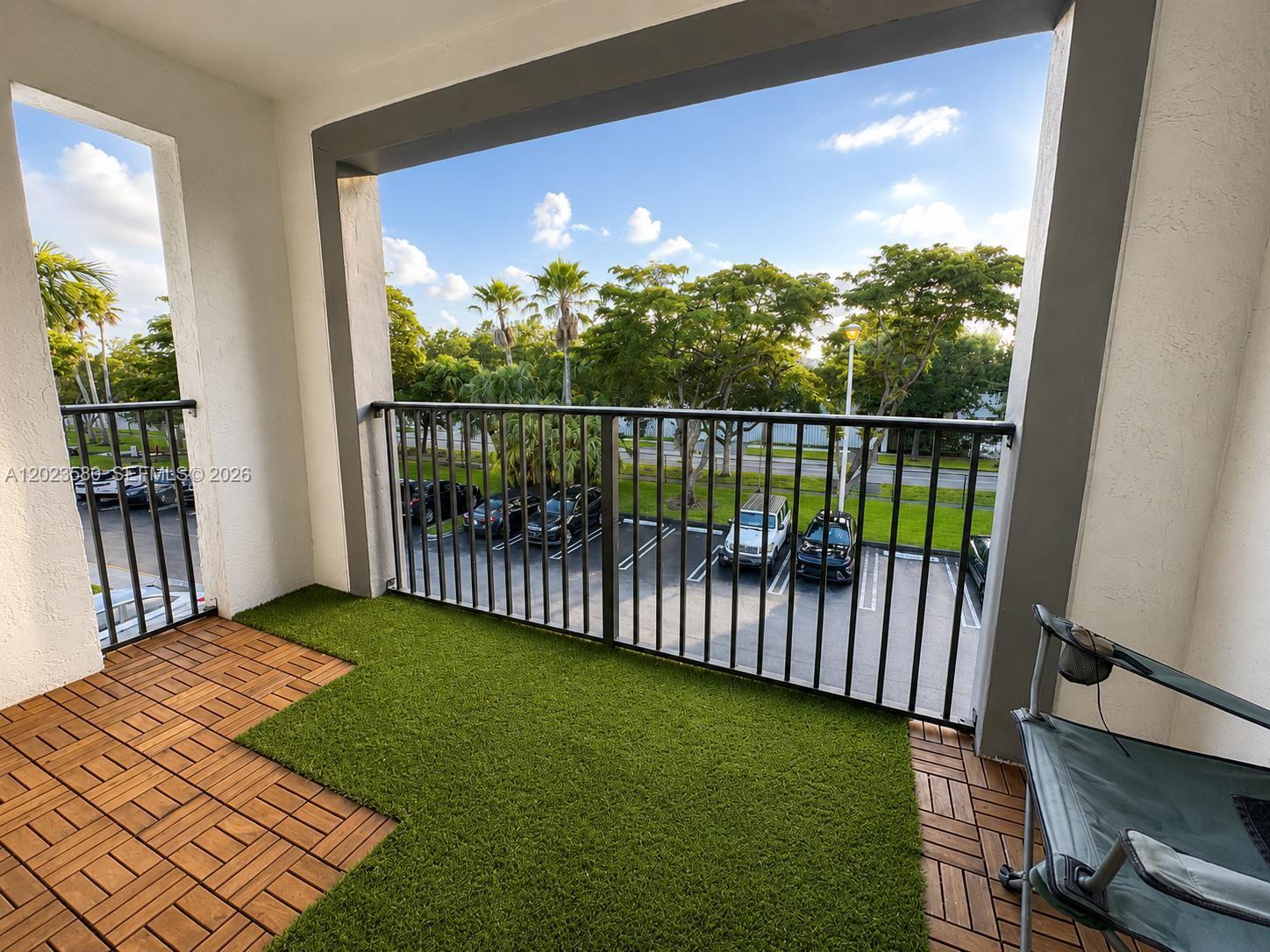 A balcony features wood-look deck tiles, artificial turf, a metal railing, and a parking lot view — 4420 NW 107th Ave # 303, Doral FL 33178, DORAL, FL