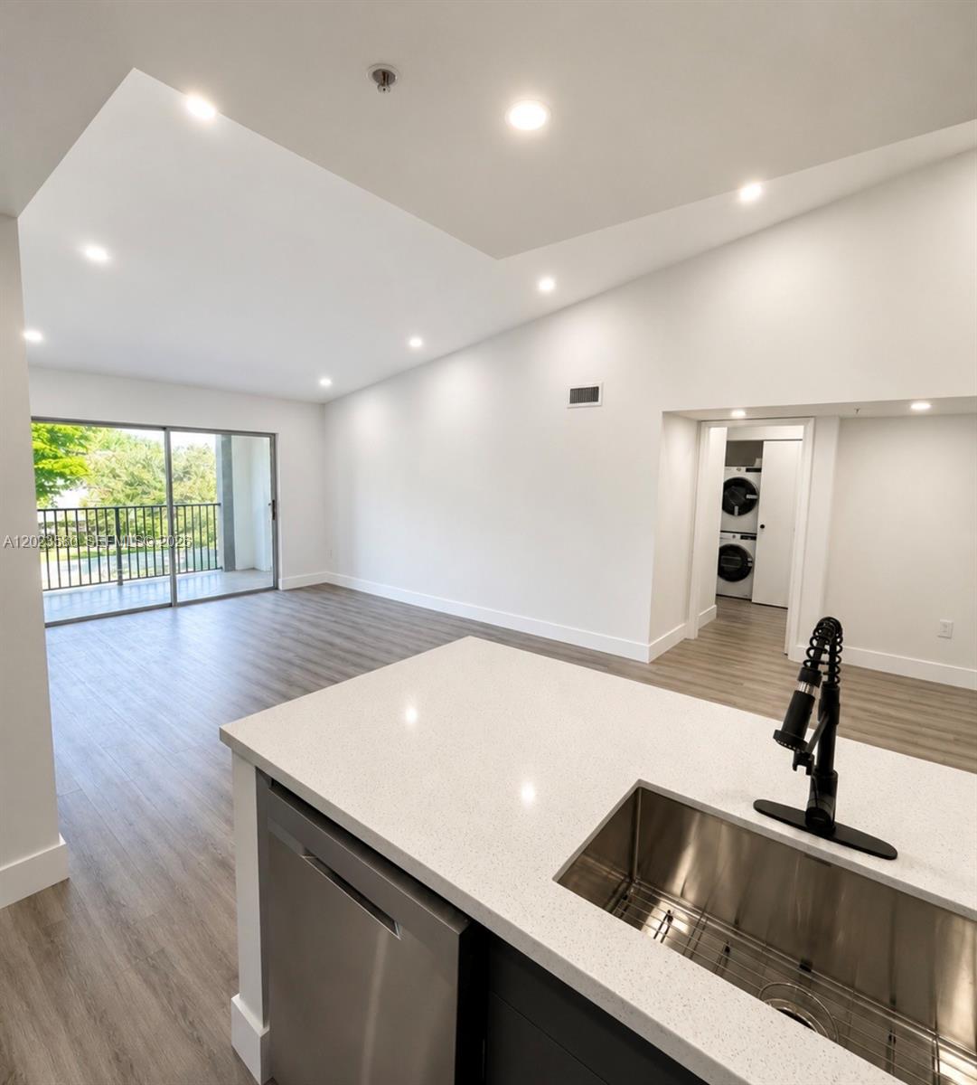 A kitchen island with a stainless steel sink overlooks an open living area with balcony access — 4420 NW 107th Ave # 303, Doral FL 33178, DORAL, FL