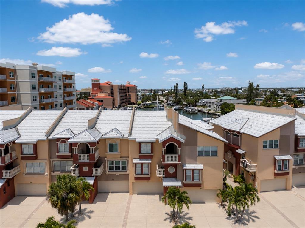 An aerial view shows a row of multi-story townhouses with white roofs and garages — 116 131ST AVENUE E UNIT F, MADEIRA BEACH, FL