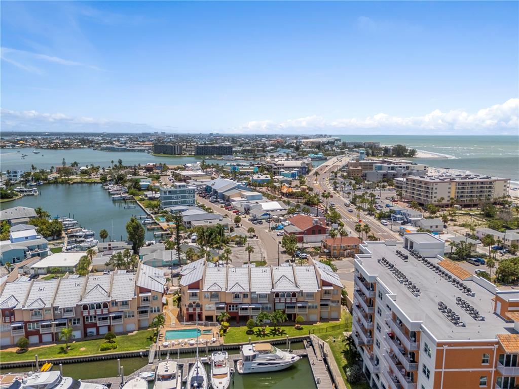 An aerial view shows a coastal town with a marina, multi-story buildings, and a bridge — 116 131ST AVENUE E UNIT F, MADEIRA BEACH, FL