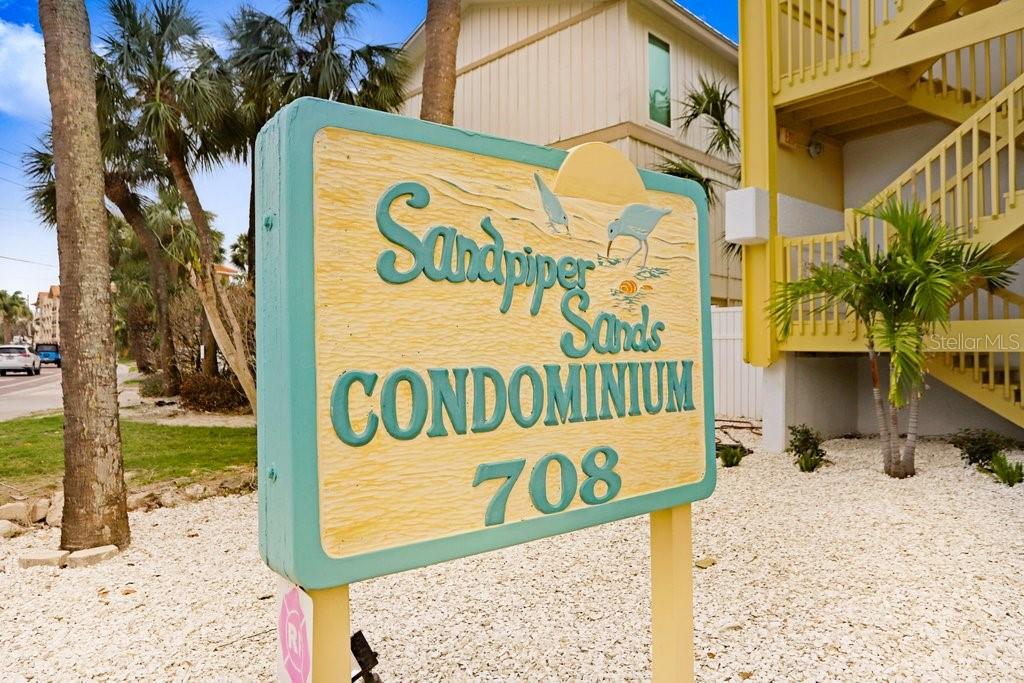 A sign for Sandpiper Sands Condominium 708 stands in a gravel area near a building — 708 GULF BOULEVARD UNIT A, INDIAN ROCKS BEACH, FL