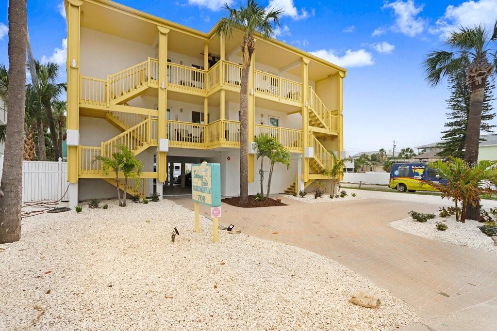 A three-story yellow apartment building features exterior wooden staircases and a gravel front yard — 708 GULF BOULEVARD UNIT A, INDIAN ROCKS BEACH, FL