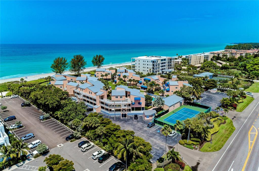 An aerial view shows a multi-story residential complex with a tennis court near the beach — 4725 GULF OF MEXICO DRIVE UNIT 314, LONGBOAT KEY, FL