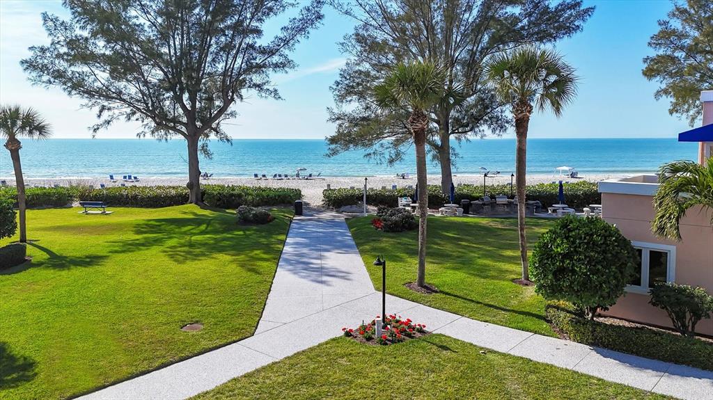 A paved walkway leads through a grassy courtyard toward a sandy beach and the ocean — 4725 GULF OF MEXICO DRIVE UNIT 314, LONGBOAT KEY, FL