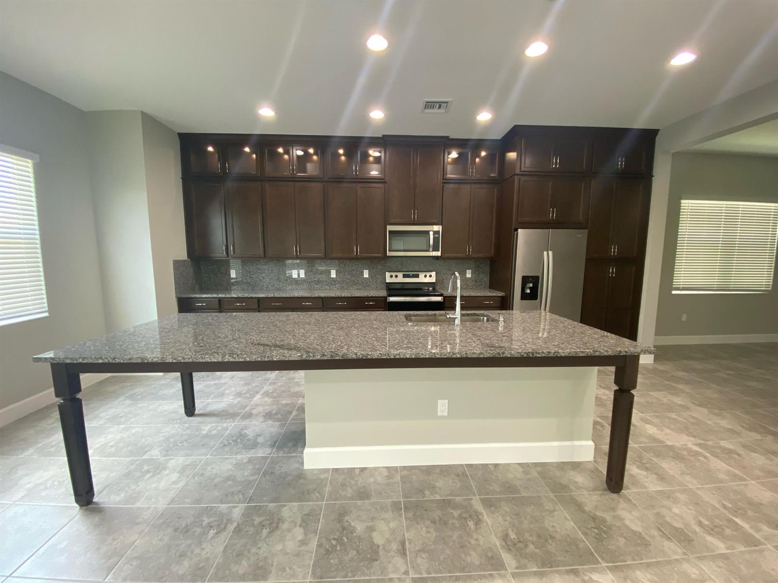 A kitchen features dark wood cabinetry, granite countertops, a large island, and tile flooring — 5383 Pecan Drive, Westlake FL 33470, WESTLAKE, FL
