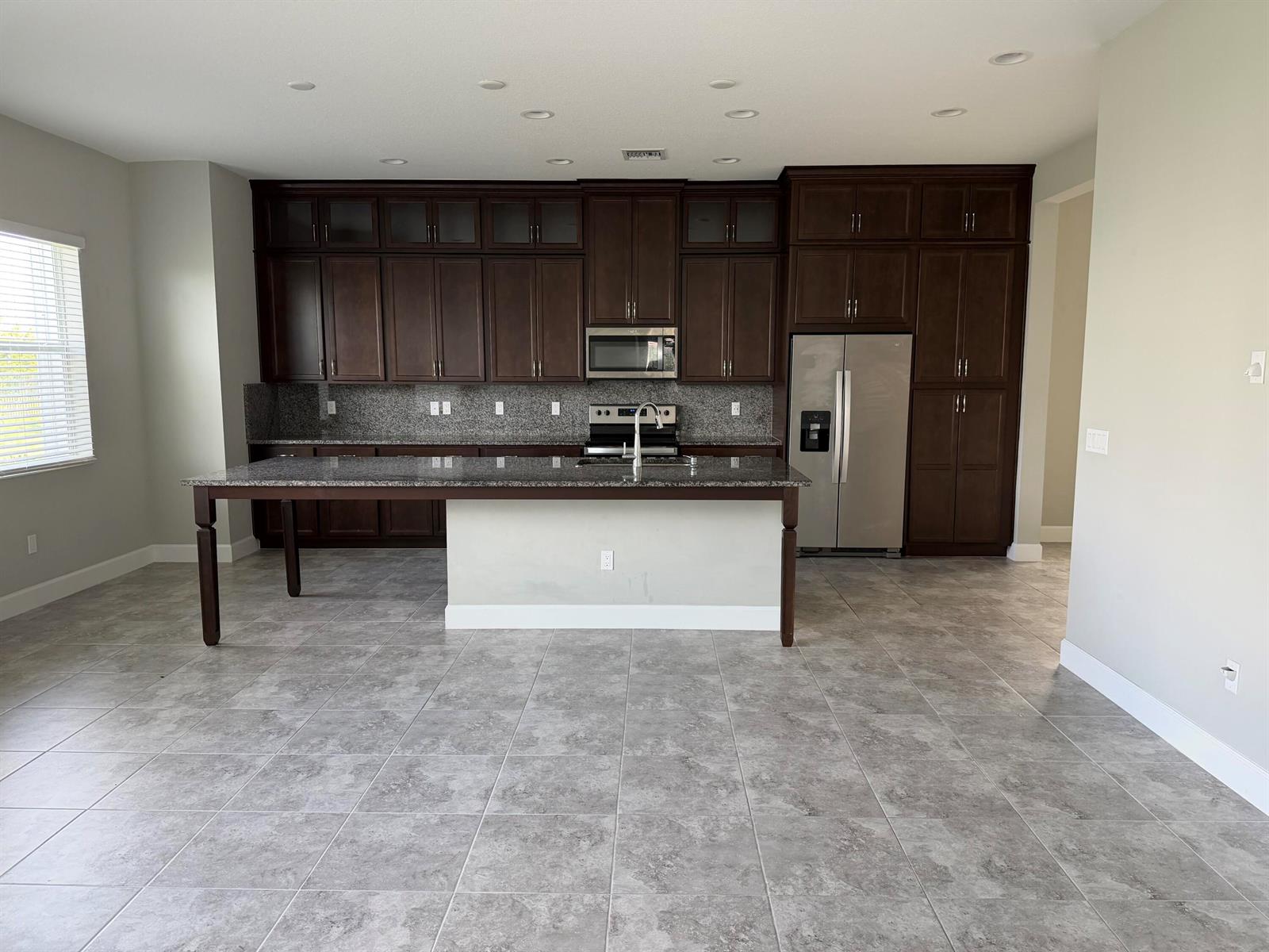 A kitchen features dark wood cabinets, granite countertops, stainless steel appliances, and gray tile flooring — 5383 Pecan Drive, Westlake FL 33470, WESTLAKE, FL