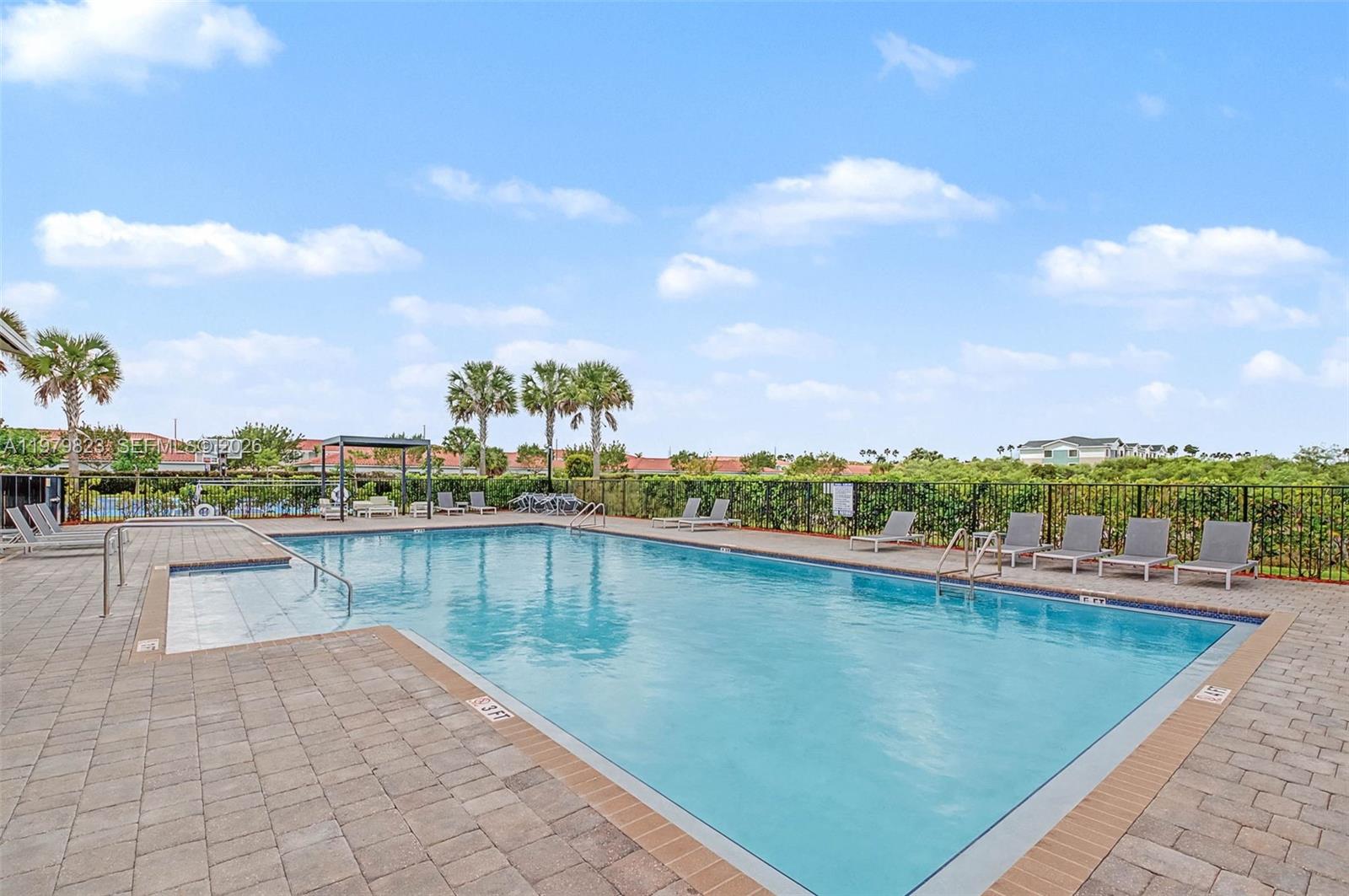 A rectangular swimming pool with lounge chairs sits on a paved patio outdoors — 445 NE 4th St, Florida City FL 33034, FLORIDA CITY, FL