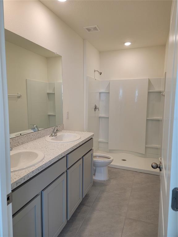 A bathroom features a double vanity with gray cabinets, a mirror, and a shower stall — 2892 EVERGREEN ELM PASS, WESLEY CHAPEL, FL