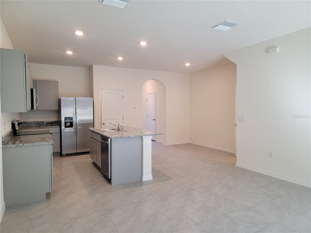 A kitchen features gray cabinets, granite countertops, a stainless steel refrigerator, and tile flooring — 2892 EVERGREEN ELM PASS, WESLEY CHAPEL, FL