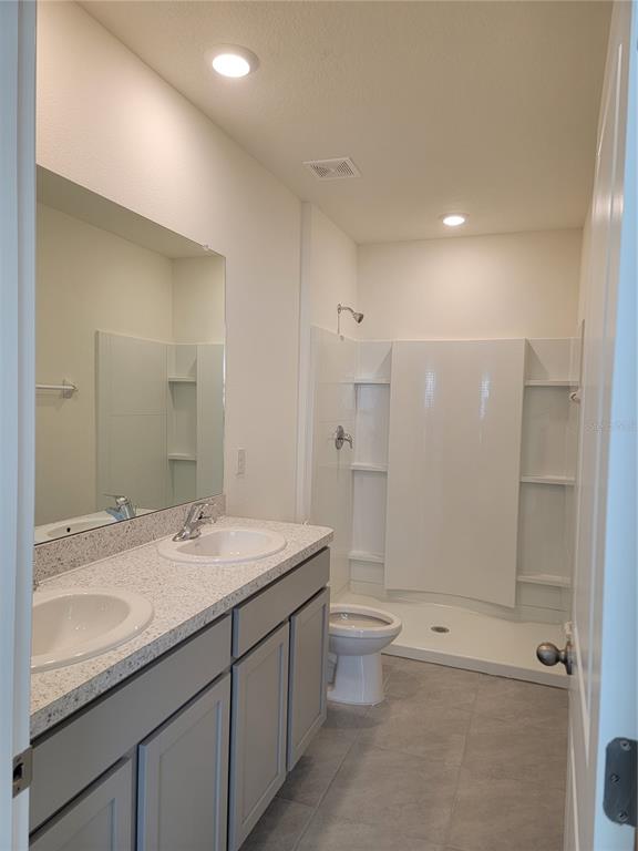 A bathroom features a double vanity with gray cabinets, a mirror, and a shower stall — 2892 EVERGREEN ELM PASS, WESLEY CHAPEL, FL