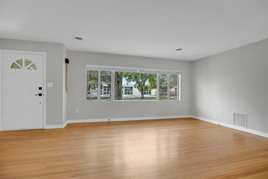 An empty room with light gray walls, hardwood floors, a white front door, and large windows — 1427 BRYN MAWR STREET, ORLANDO, FL