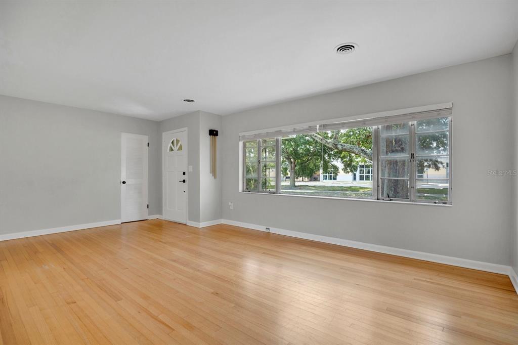 An empty living room features light hardwood floors, gray walls, and a large picture window — 1427 BRYN MAWR STREET, ORLANDO, FL