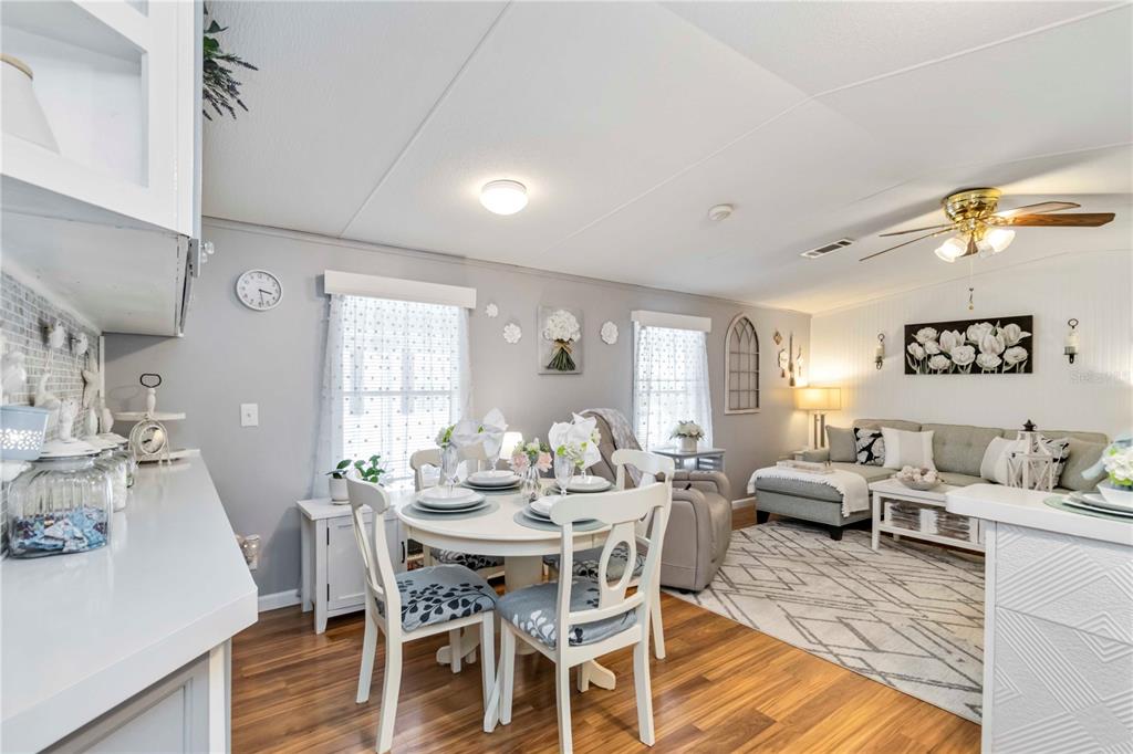 An open-concept living and dining area features light gray walls, wood flooring, and white furniture — 10303 BURNT STORE ROAD UNIT 230, PUNTA GORDA, FL