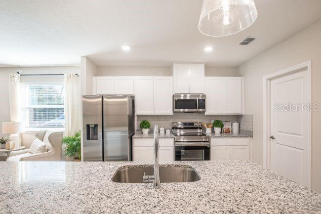 A modern kitchen features white cabinets, stainless steel appliances, and a granite-topped island with sink — 8 ROXBURY LANE, PALM COAST, FL