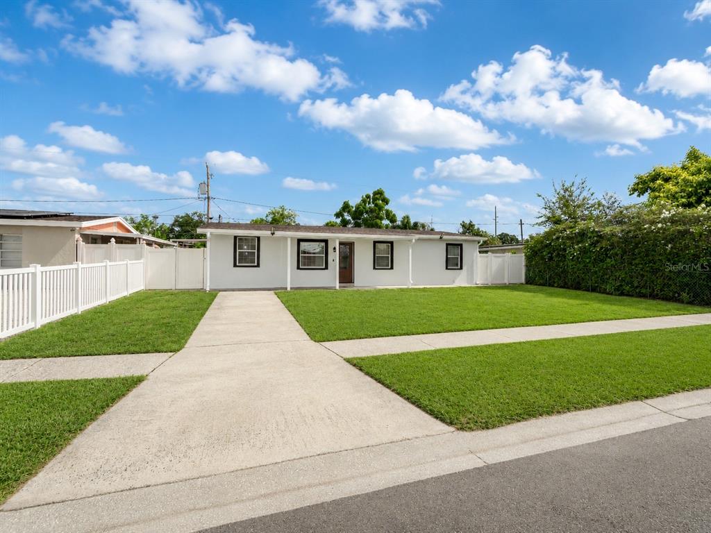 A single-story white house with a concrete driveway and a green lawn under a blue sky — 4409 W HANNA AVENUE, TAMPA, FL