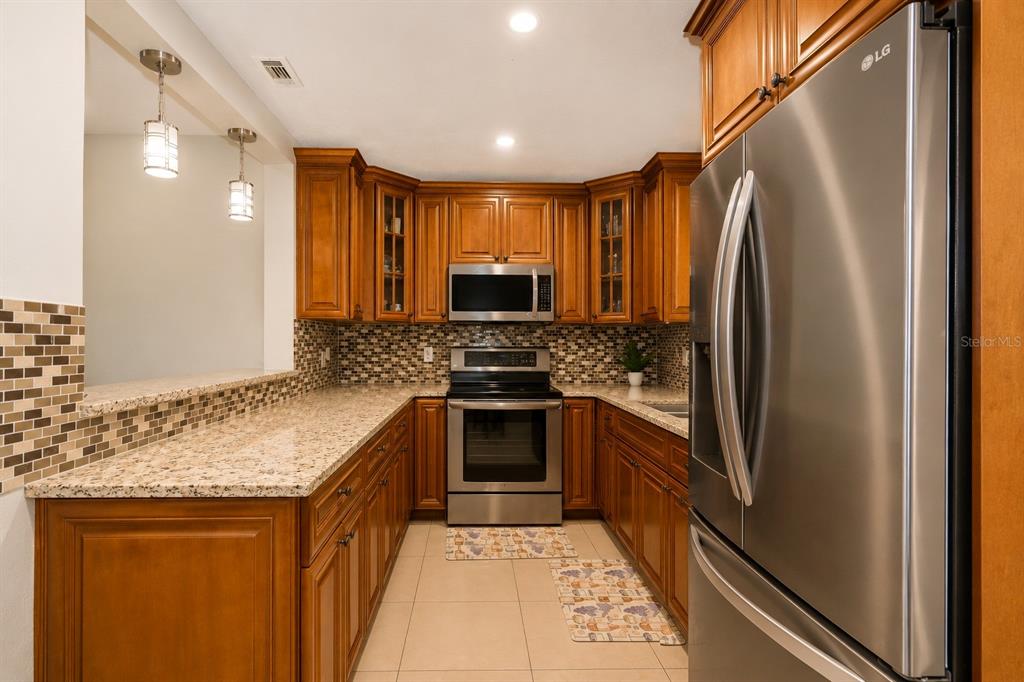 A kitchen with wood cabinets, granite countertops, stainless steel appliances, and a tiled backsplash — 4409 W HANNA AVENUE, TAMPA, FL