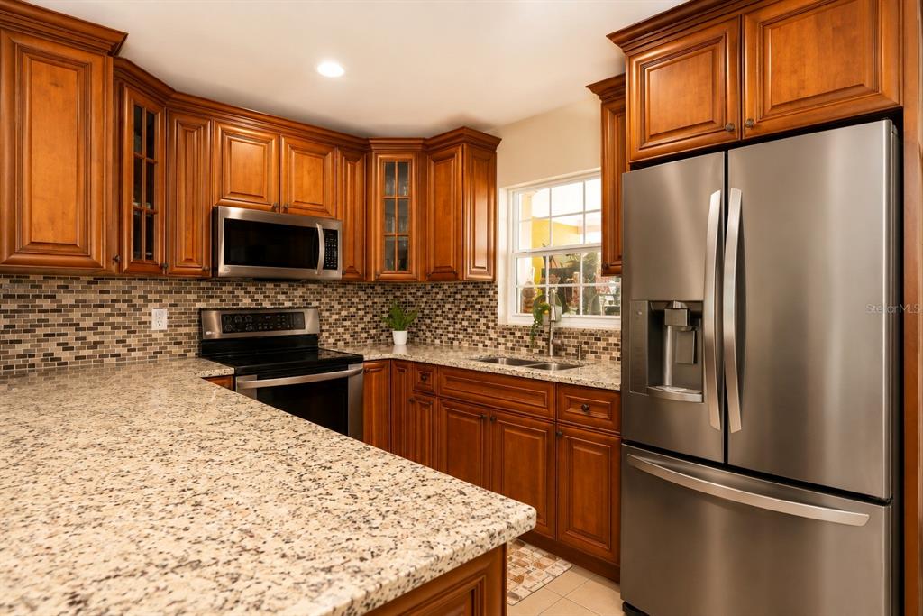 A kitchen with wood cabinets, granite countertops, stainless steel appliances, and a tiled backsplash — 4409 W HANNA AVENUE, TAMPA, FL
