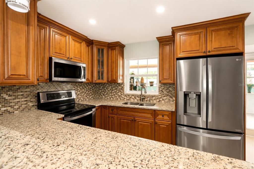 A kitchen features wood cabinets, granite countertops, stainless steel appliances, and a tiled backsplash — 4409 W HANNA AVENUE, TAMPA, FL