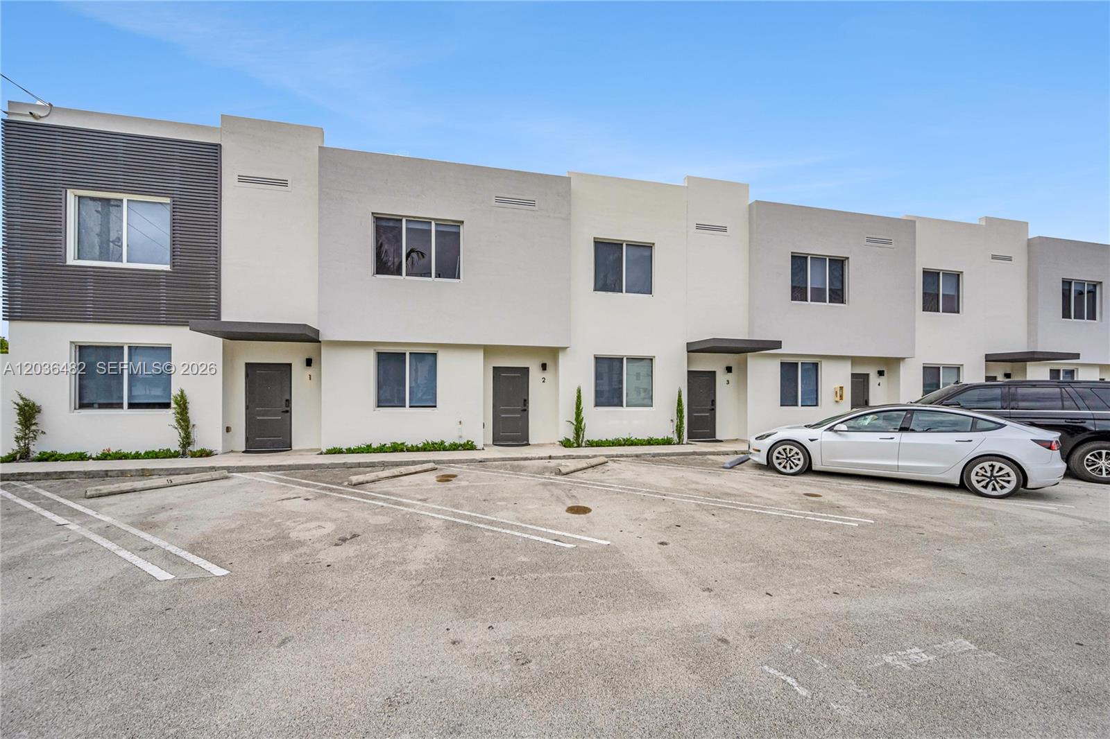 A row of modern two-story townhouses features gray doors and a paved parking lot — 170 NW 158th St # 2, Miami FL 33169, MIAMI, FL