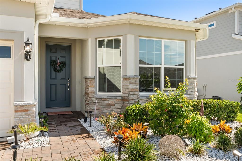 The exterior of a house features a blue front door, stone siding, and landscaped garden — 4708 WEATHERBELL ROAD, WINTER GARDEN, FL