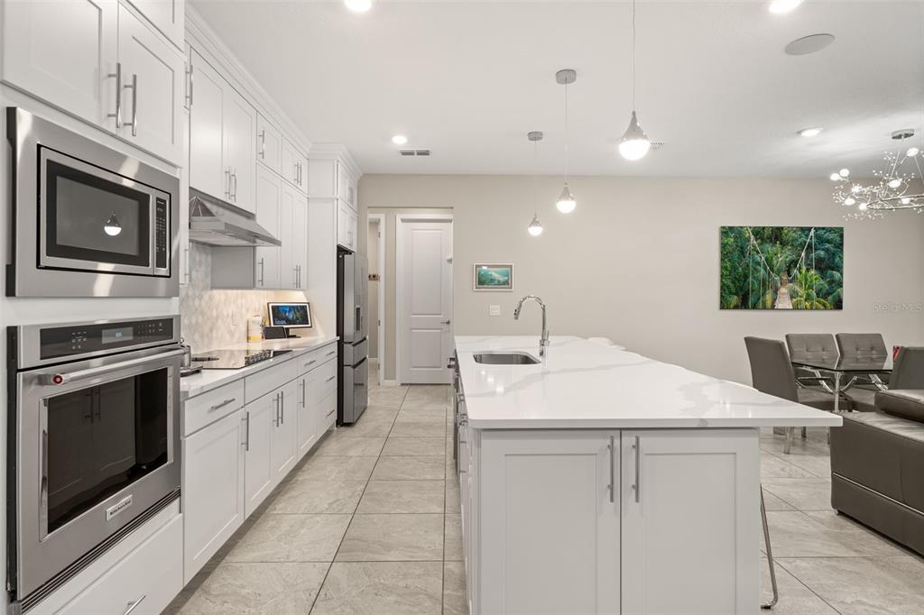A modern kitchen features white cabinetry, stainless steel appliances, a large island, and tile flooring — 4708 WEATHERBELL ROAD, WINTER GARDEN, FL