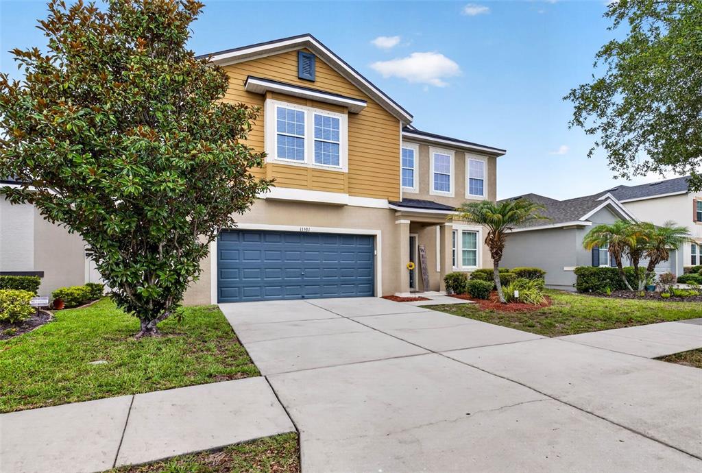 A two-story house with a yellow-sided upper level, a beige stucco lower level, and a garage — 11531 TANGLE BRANCH LANE, GIBSONTON, FL