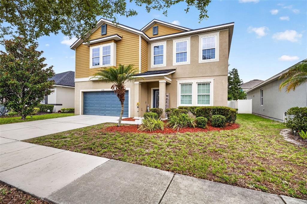 A two-story house with a blue garage door, yellow siding, and a concrete driveway — 11531 TANGLE BRANCH LANE, GIBSONTON, FL