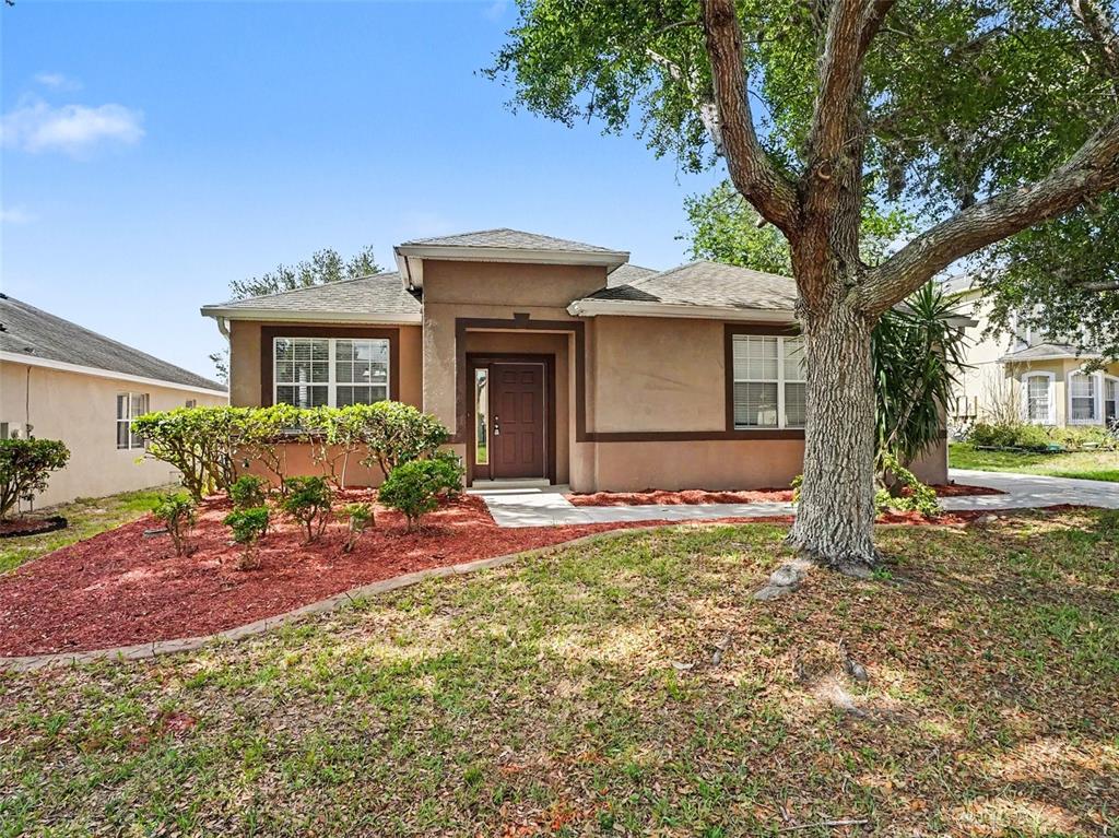 A tan, single-story stucco house with a brown front door and a large tree — 1942 BEARDSLEY DRIVE, APOPKA, FL