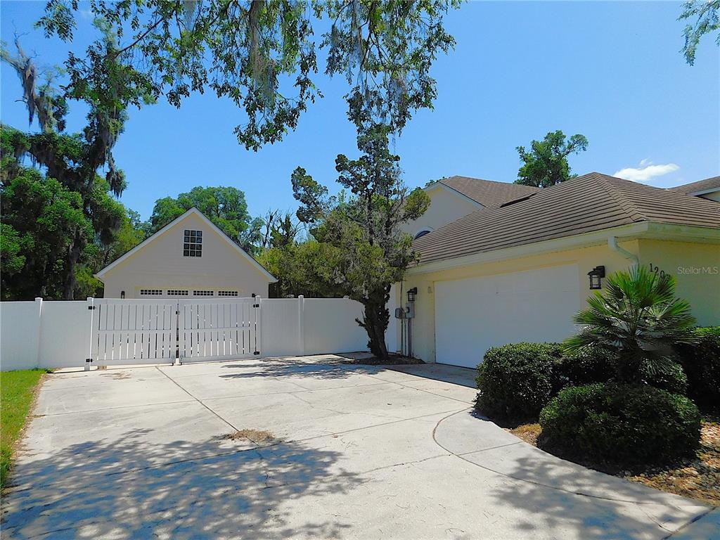 A white vinyl fence and gate stand in front of a detached garage and house — 1203 SE 49TH AVENUE, OCALA, FL