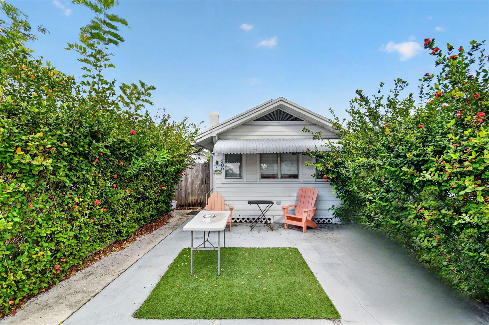 A small white house features a patio with a table, chairs, and a grass rug — 306 N J Street, FL 33460, FL