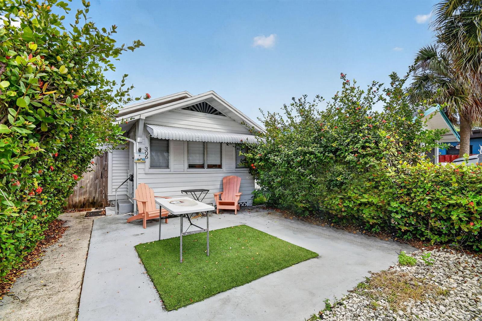 A small, light-gray cottage features a concrete patio with a folding table and two chairs — 306 N J Street, FL 33460, FL